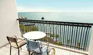 En balkon med et bord, stol og stribet håndklæde, med havudsigt. (AI-genereret tekst)