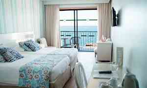 Et hotelværelse med en seng, et skrivebord og udsigt over havet fra en altan. (AI-genereret tekst)