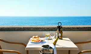 Udsigt over havet fra en terrasse med et dækket bord med mad og drikke. (AI-genereret tekst)