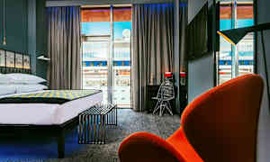 Moderne hotelværelse med stor seng, skrivebord og stol samt udsigt gennem store vinduer. (AI-genereret tekst)