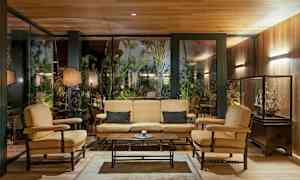 Interiør med siddegruppe bestående af sofa og lænestole foran en glasvæg med vegetation udenfor. (AI-genereret tekst)