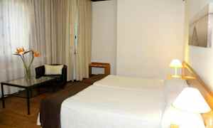 Et hotelværelse med to senge, en lænestol og et bord med en blomsteropsats. (AI-genereret tekst)