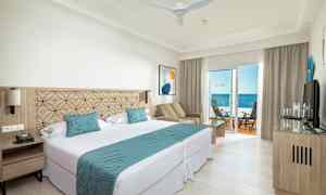 Et hotelværelse med dobbeltseng, siddeområde og balkon med havudsigt. (AI-genereret tekst)