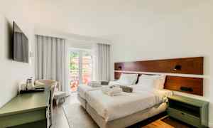 Et hotelværelse med to enkeltsenge, hvidt sengetøj og puder. Værelset har en balkon med udsigt og er indrettet med et skrivebord og et tv. (AI-genereret tekst)
