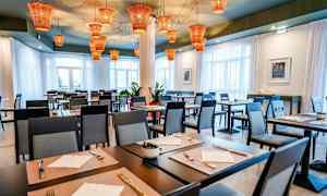 Restaurant med dækkede borde og moderne stole, med orange lamper i loftet. (AI-genereret tekst)