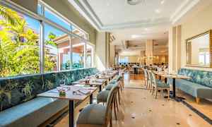 En lys restaurant med moderne borde og stole samt store vinduer med udsigt til grønne omgivelser. (AI-genereret tekst)