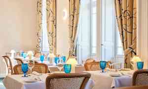 Billede af en elegant restaurant med dækkede borde, blå glas og varm belysning. (AI-genereret tekst)