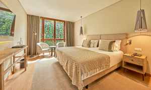 Et hotelværelse med en bred seng, to lænestole ved et vindue og et bord. (AI-genereret tekst)