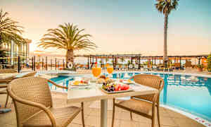 Et morgenmadsbord ved en pool med solsenge og palmer i baggrunden. (AI-genereret tekst)