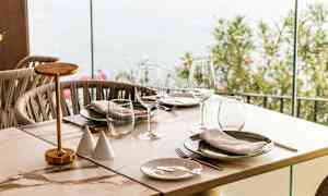 Et dækket bord med glas og tallerkener ved siden af en glasvæg der vender udendørs. (AI-genereret tekst)