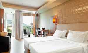 Hotelværelse med to enkeltsenge, siddegruppe og udsigt til et bjergrigt område gennem glasdøren. (AI-genereret tekst)