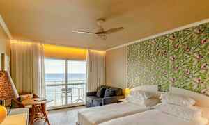 Et hotelværelse med to senge, en mønstret grøn tapetvæg og en altan med udsigt over havet. (AI-genereret tekst)