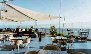 Udendørsterrasse med borde og stole, pergola og havudsigt. (AI-genereret tekst)