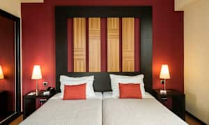 To senge med hvidt sengetøj og røde puder, en væg med træpaneler og rød baggrund. (AI-genereret tekst)