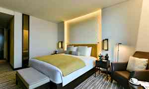 Et moderne hotelværelse med en dobbeltseng, to natborde og en komfortabel lænestol. (AI-genereret tekst)