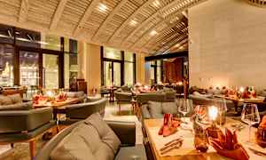 En elegant restaurant med bjælkeloft, dækkede borde med orange servietter og hyggelig belysning. (AI-genereret tekst)