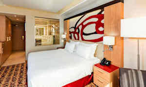 Et moderne hotelværelse med en stor seng og en gennemsigtig glasvæg mod et badeværelse. (AI-genereret tekst)