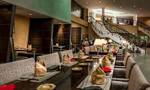 En elegant restaurant med borde dækket med servietter og tallerkener samt en trappe i baggrunden. (AI-genereret tekst)