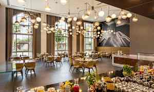 En elegant restaurant med moderne hængelamper, dækkede borde og store vinduer, der lukker naturligt lys ind. (AI-genereret tekst)