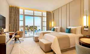 Et hotelværelse med to enkeltsenge, skrivebord, lænestol og balkon med udsigt over omgivelserne. (AI-genereret tekst)