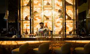 En smukt oplyst bardisk med stole i forgrunden og hylder med pynt i baggrunden. (AI-genereret tekst)