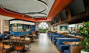 En restaurant med borde, stole og blå sofaer samt en bar i baggrunden. (AI-genereret tekst)