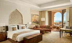 Et hotelværelse med en dobbeltseng, siddeområde, skrivebord og altan med havudsigt. (AI-genereret tekst)