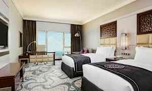 Et hotelværelse med to senge, skrivebord og udsigt over havet. Vægsdekoration og elegant indretning. (AI-genereret tekst)