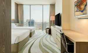 Et hotelværelse med to senge, skrivebord, stol og TV. Vindue med udsigt over en by. (AI-genereret tekst)