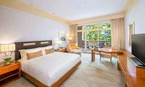 Et hotelværelse med en stor seng, et skrivebord og en balkon med udsigt til grønne omgivelser. (AI-genereret tekst)