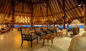 Et luksuriøst siddeområde med træstole og sofaer, elegant belysning og udsigt over havet gennem åbne vægge. (AI-genereret tekst)