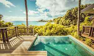 Udsigt fra en træterrasse og en pool over en tropisk have og havet. (AI-genereret tekst)