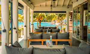 Udendørsservering med udsigt til havet, møbler med grå hynder. (AI-genereret tekst)