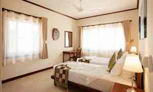 Et hotelværelse med to enkeltsenge med hvide lagner og dekorative sengeklæder, skrivebord med spejl og store vinduer med gardiner. (AI-genereret tekst)