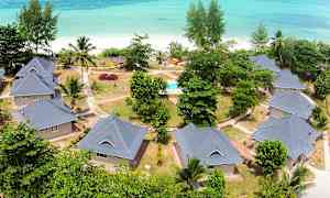 Luftfoto af bolighuse med haver og gangstier nær en strand med turkis hav. (AI-genereret tekst)