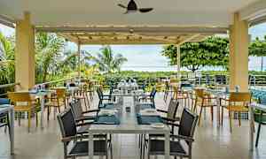 En udendørs restaurant med borde og stole omgivet af grønt og udsigt til havet. (AI-genereret tekst)