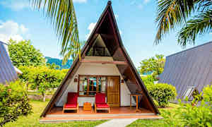 Et A-formet træhus med to liggestole foran, omringet af grønt. (AI-genereret tekst)