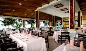 Billede af en restaurant med opdækkede borde og udsigt til et frodigt udendørsmiljø. (AI-genereret tekst)