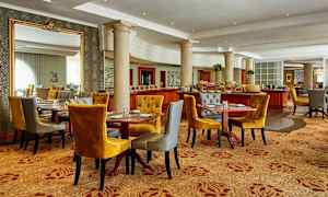 Et elegant spiseområde med flere opdækkede borde, komfortable stole i sennepsgul og grå farve samt dekorative søjler og spejle. (AI-genereret tekst)