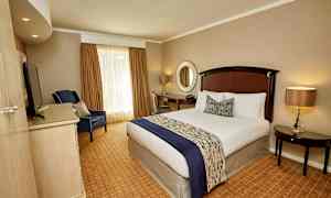 Et hotelværelse med en redt seng, en lænestol, et skrivebord og et rundt spejl på væggen. (AI-genereret tekst)