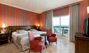 Dobbeltværelse med to røde lænestole, et bord, havudsigt fra en balkon. (AI-genereret tekst)