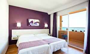 Værelse med dobbeltseng, lilla væg og altan med havudsigt. (AI-genereret tekst)