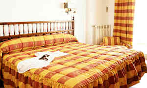 Et hotelværelse med en seng med et gul og orange ternet sengetæppe. (AI-genereret tekst)