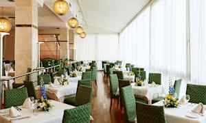 Et lyst og elegant indrettet spiseområde med grønne stole og hvide duge på bordene, dekoreret med friske blomsterarrangementer. (AI-genereret tekst)