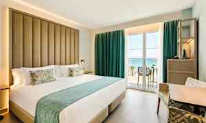 Hotelværelse med stor seng og balkon med havudsigt. (AI-genereret tekst)