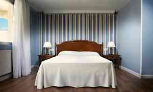 Hotelværelse med seng i midten, to natborde med lamper og blåstribet tapet. (AI-genereret tekst)