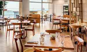 Moderne borde og stole i træ i en restaurant med havudsigt. (AI-genereret tekst)