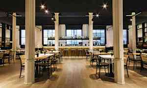 En elegant restaurant med borde og stole samt en veloplyst bardisk i baggrunden. (AI-genereret tekst)