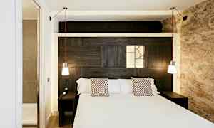 Et hotelværelse med en dobbeltseng, to hængende lamper og et indbygget lysfelt på trævæggen bag sengen. (AI-genereret tekst)