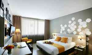 Et moderne hotelværelse med en dobbeltseng dækket af hvidt og gult sengetøj. I rummet er der et skrivebord med en blomsterkrukke og lamper på natbordene. (AI-genereret tekst)